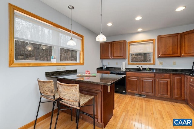kitchen with a sink, black dishwasher, a breakfast bar, pendant lighting, and light wood-style flooring