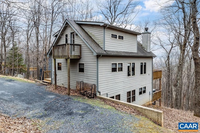 rear view of house featuring a shingled roof, a chimney, and a balcony