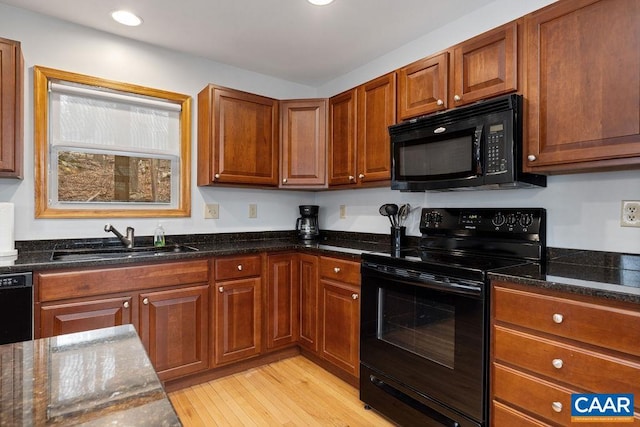 kitchen with dark stone countertops, a sink, black appliances, light wood-style floors, and recessed lighting