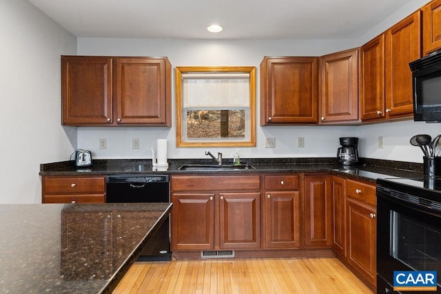 kitchen with a sink, black appliances, visible vents, and dark stone counters