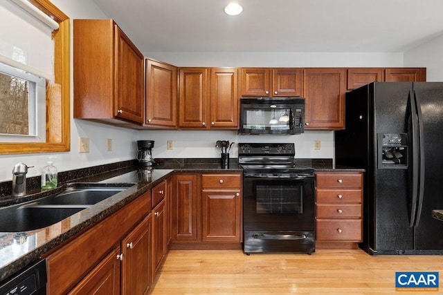 kitchen with black appliances, light wood-style floors, dark stone countertops, and a sink