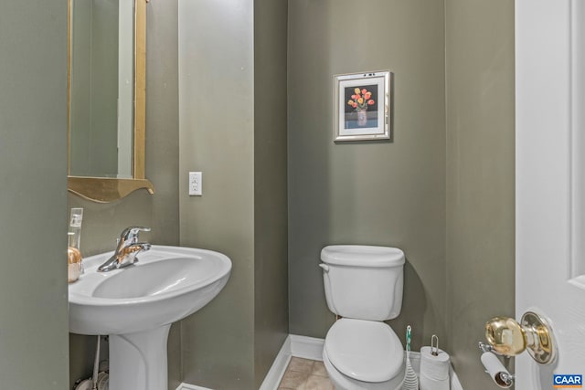 half bathroom with toilet, baseboards, tile patterned flooring, and a sink