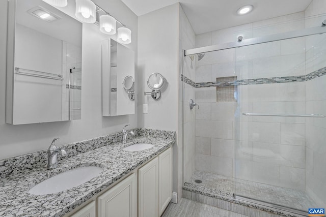 full bathroom with a stall shower, double vanity, and a sink