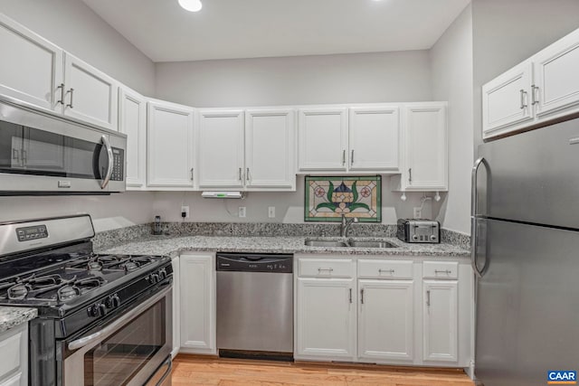 kitchen with a sink, stainless steel appliances, white cabinetry, and light stone countertops