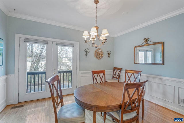 dining room featuring a notable chandelier, a decorative wall, crown molding, and wainscoting