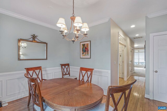 dining area with a notable chandelier, visible vents, crown molding, a wainscoted wall, and light wood-type flooring