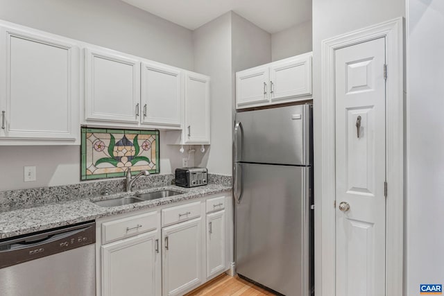 kitchen with a sink, stainless steel appliances, light wood-type flooring, light stone counters, and white cabinetry