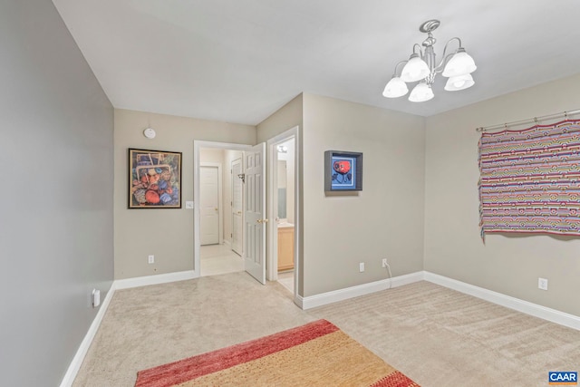 unfurnished bedroom with baseboards, ensuite bathroom, a chandelier, and light colored carpet