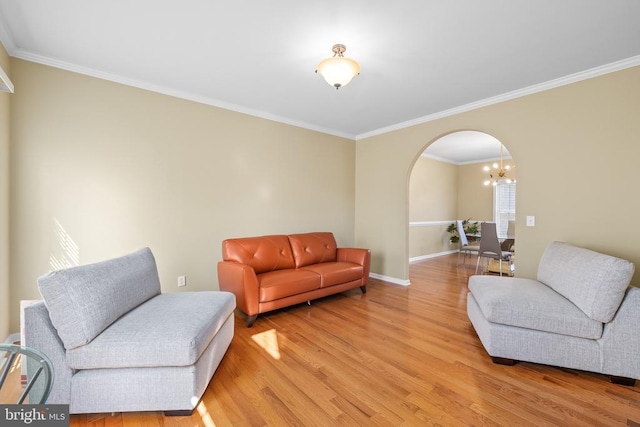 living room featuring arched walkways, light wood finished floors, crown molding, baseboards, and a chandelier