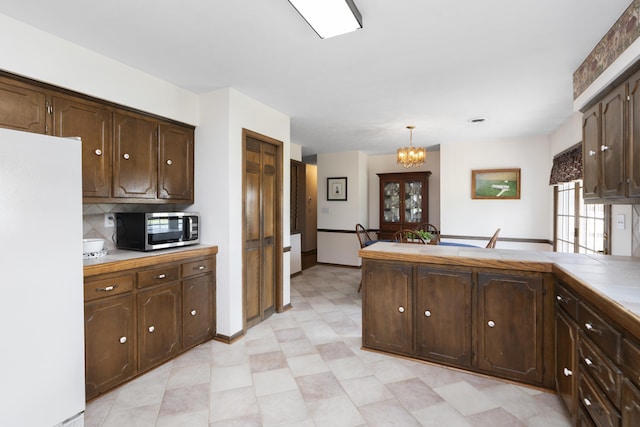 kitchen featuring freestanding refrigerator, stainless steel microwave, dark brown cabinets, and a chandelier