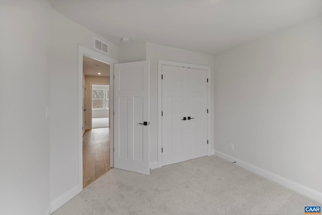 unfurnished bedroom with baseboards, light carpet, a closet, and visible vents