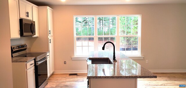 kitchen with appliances with stainless steel finishes, white cabinetry, sink, dark stone counters, and light hardwood / wood-style flooring