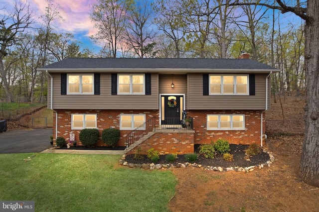 - split foyer home with brick siding, a chimney, and a yard