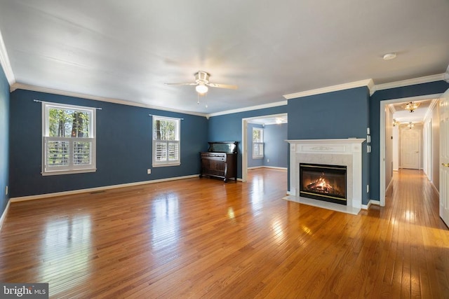  - unfurnished living room featuring ceiling fan, ornamental molding, hardwood / wood-style floors, plenty of natural light, and a high end fireplace