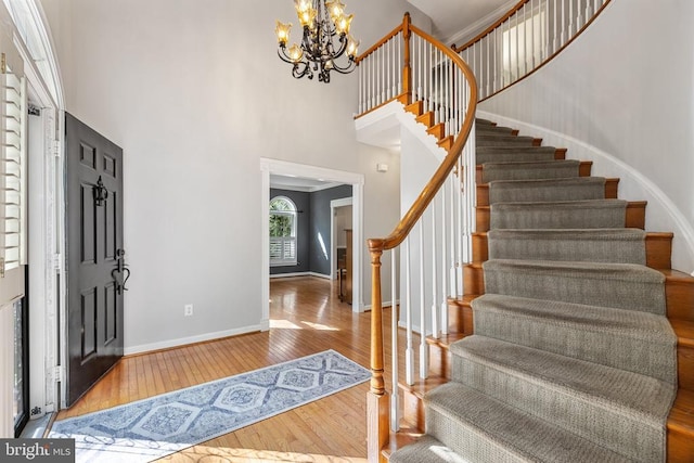  - foyer featuring stairs, a towering ceiling, wood-type flooring, a chandelier, and baseboards