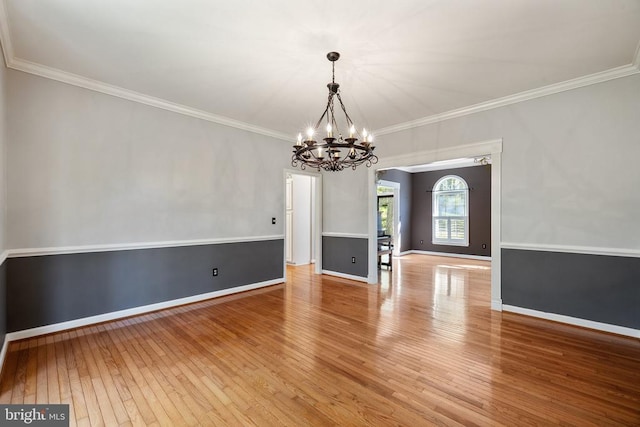  - empty room with a chandelier, hardwood / wood-style floors, ornamental molding, and baseboards