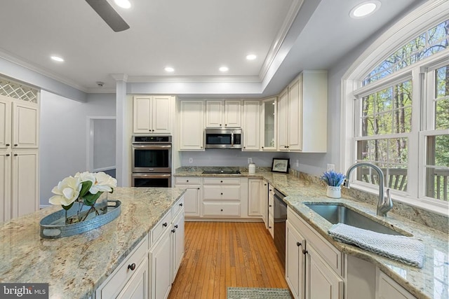  - kitchen with appliances with stainless steel finishes, crown molding, light wood-style floors, a sink, and light stone counters