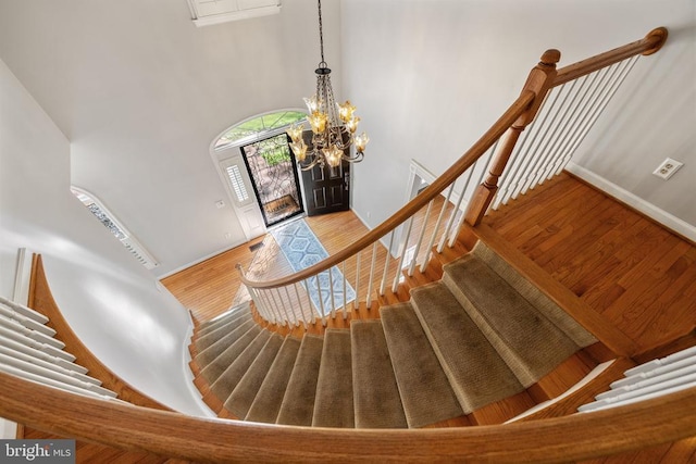  - staircase with a chandelier, wood finished floors, baseboards, and a high ceiling