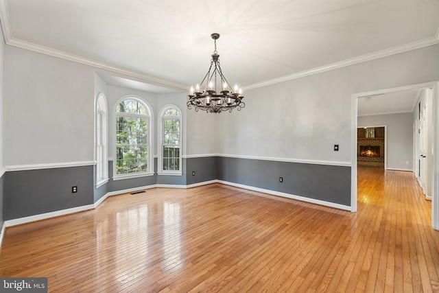  - unfurnished room with wood-type flooring, a chandelier, ornamental molding, baseboards, and a fireplace