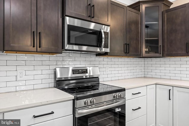 12521 Wilderness Park Dr, Spotsylvania, VA 22551 - kitchen with appliances with stainless steel finishes, dark brown cabinetry, light stone counters, glass insert cabinets, and tasteful backsplash