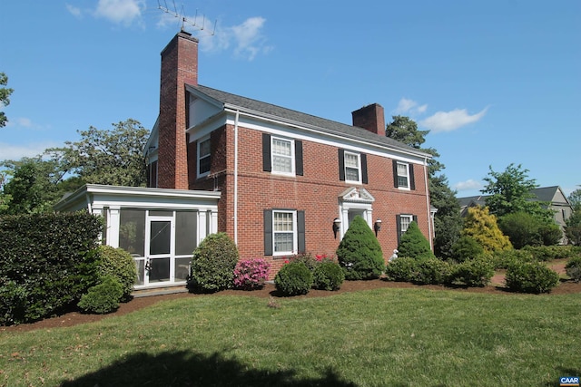 colonial inspired home with a chimney, a front lawn, brick siding, and a sunroom