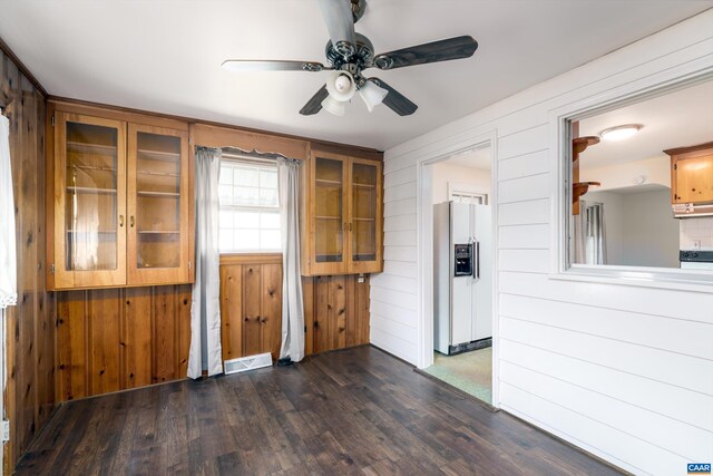 unfurnished room featuring wooden walls, a ceiling fan, dark wood-type flooring, and visible vents