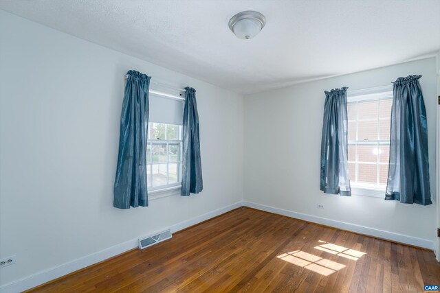 empty room with baseboards, visible vents, and dark wood finished floors