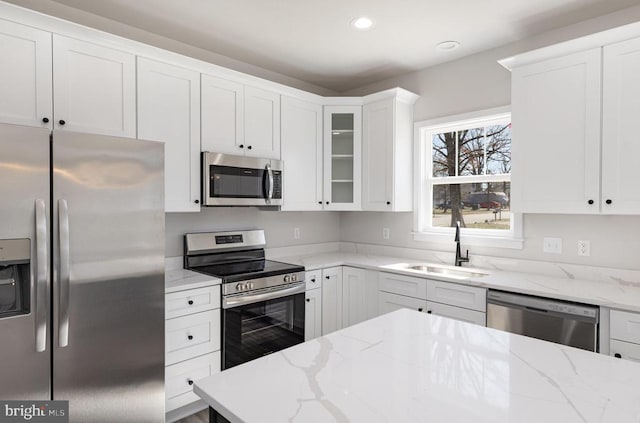 kitchen featuring appliances with stainless steel finishes, a sink, white cabinets, light stone countertops, and recessed lighting