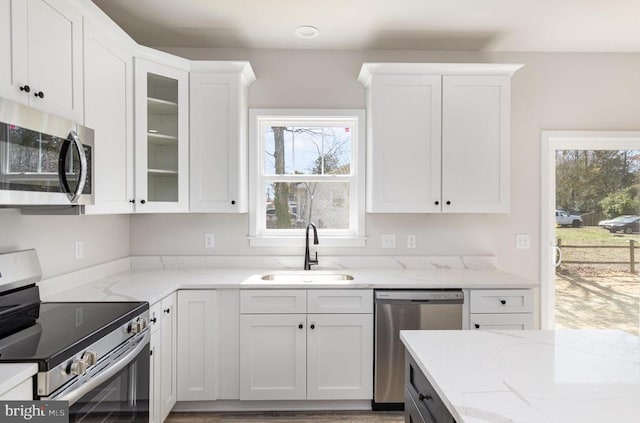 kitchen featuring appliances with stainless steel finishes, a sink, white cabinets, and light stone countertops