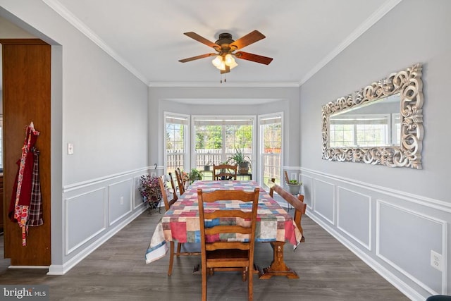 dining room featuring a decorative wall, ceiling fan, wood finished floors, ornamental molding, and a wainscoted wall