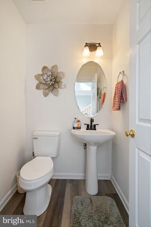 half bathroom with wood finished floors, toilet, and baseboards