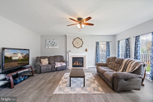 living room with wood finished floors, ceiling fan, a fireplace with flush hearth, and baseboards