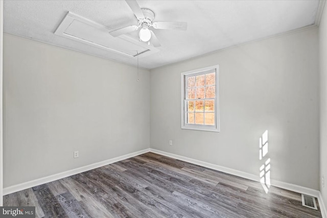 empty room with attic access, ceiling fan, wood finished floors, baseboards, and ornamental molding