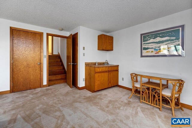 kitchen with brown cabinetry, light colored carpet, baseboards, a textured ceiling, and a sink