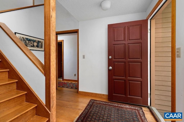 entrance foyer with wood finished floors, a textured ceiling, stairs, and baseboards