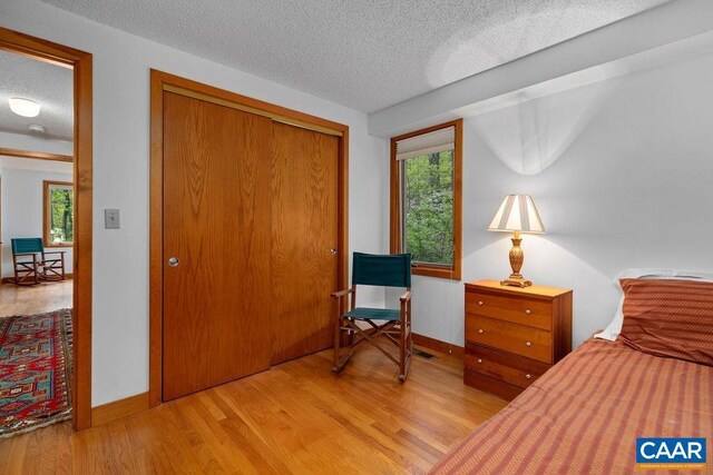 bedroom featuring light wood-type flooring, a textured ceiling, multiple windows, baseboards, and a closet