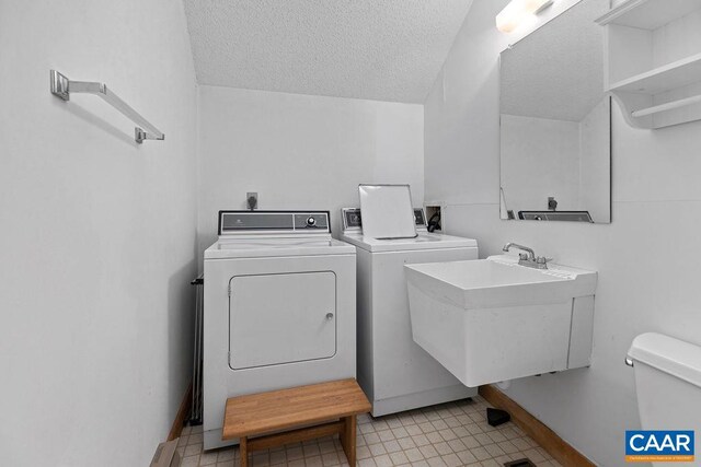 laundry area featuring washer and clothes dryer, a sink, a textured ceiling, and baseboards