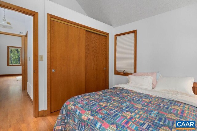 bedroom with light wood-style flooring, a closet, lofted ceiling, and a textured ceiling
