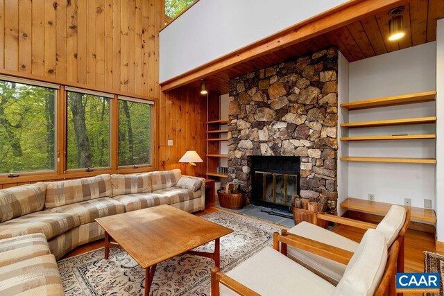 living area featuring wood finished floors, a stone fireplace, wooden walls, a high ceiling, and beamed ceiling