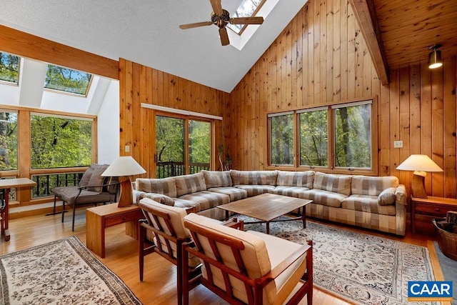 living area with a skylight, healthy amount of natural light, wooden walls, high vaulted ceiling, and light wood-style floors