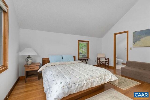 bedroom featuring lofted ceiling, light wood finished floors, and ensuite bath