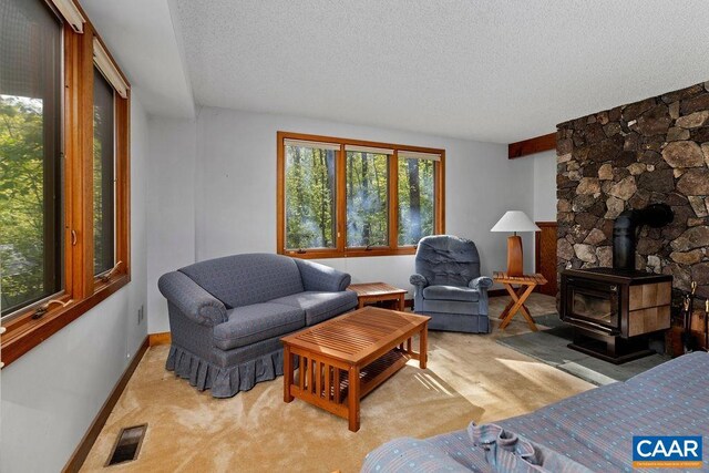 living area with a textured ceiling, a wood stove, baseboards, and light colored carpet