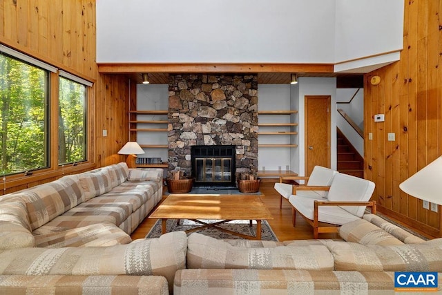 living area with wooden walls, wood finished floors, stairway, a high ceiling, and a stone fireplace