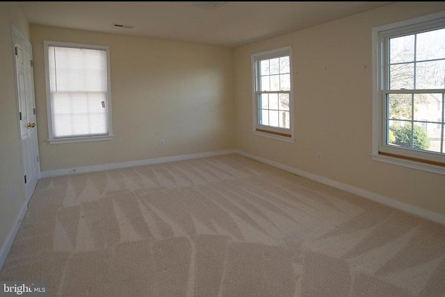 empty room featuring healthy amount of natural light, light colored carpet, and baseboards