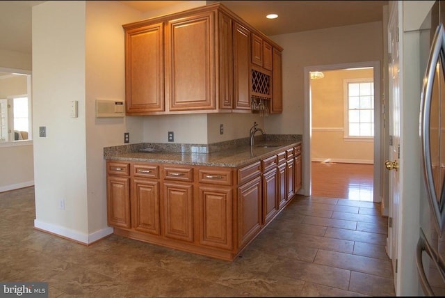 kitchen featuring a sink, stainless steel fridge, brown cabinetry, baseboards, and recessed lighting