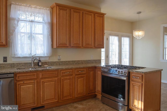 kitchen featuring stainless steel appliances, a sink, a peninsula, brown cabinets, and light stone countertops