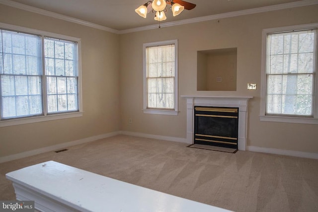 unfurnished living room featuring ceiling fan, crown molding, carpet flooring, a fireplace with flush hearth, and healthy amount of natural light