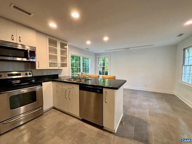 kitchen featuring stainless steel appliances, a sink, a peninsula, dark countertops, and recessed lighting