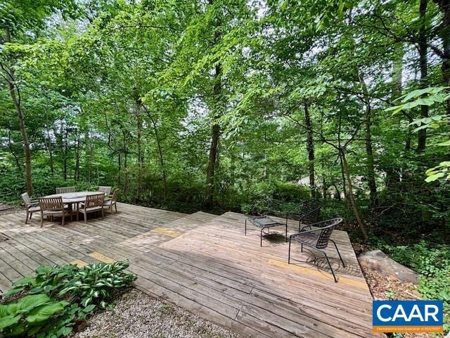 wooden deck featuring outdoor dining space and a wooded view