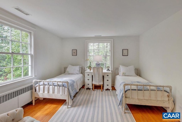 bedroom with radiator, multiple windows, and wood finished floors